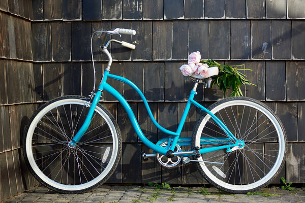 Close-up of blue vintage bicycle with bouquet of gently pink peonies on dark wall background