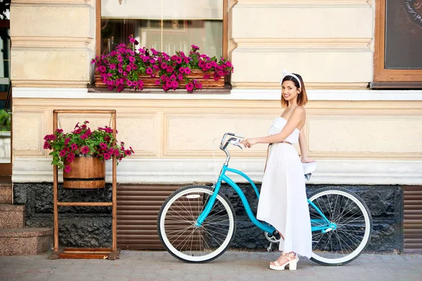 街で自転車と一緒にポーズをしながら笑みを浮かべて美しい幸せな若い女 — ストック写真