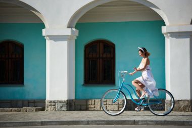 gülümseyen güzel kadın önünde turkuaz mavi bisiklet sürme beyaz uzun elbiseli duvar eski şehri güneşli yaz gününde bina