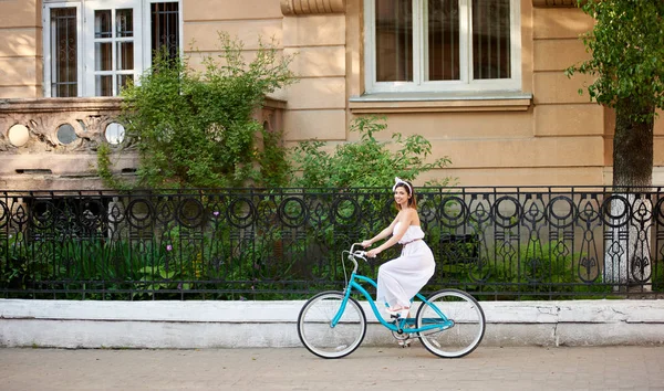 可爱的女人穿着轻礼服在老式自行车骑沿城市街道 — 图库照片