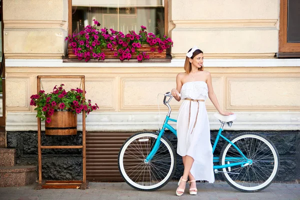 街で自転車と一緒にポーズをしながら笑みを浮かべて美しい幸せな若い女 — ストック写真