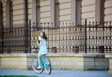 Gülümseyen güzel kadın geri süre çiçek tutan ve metal çit ile oldukça tarihi şehir aşağı mavi bisiklet sürme arıyorum. Oldukça olumlu kız turkuaz Bisiklet mutlu sevinç yaz güneşli gün