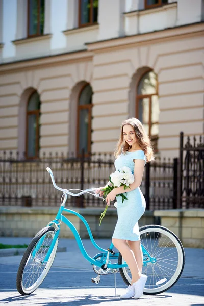 ゴージャスなセクシーな若い女性彼女は自転車で 花の束を持って市内中心で優雅にポーズをとってカメラに笑顔 — ストック写真