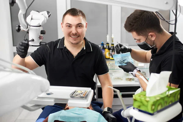 男性牙医与陶瓷大括号是微笑的相机 而另一个是使用医疗器械 — 图库照片