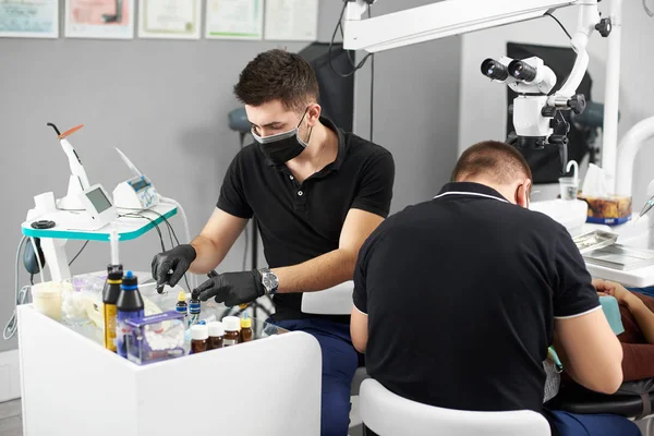 年轻的助手在一个黑色的面具和手套帮助牙医在治疗过程中的病人 现代牙科与新技术的应用 — 图库照片