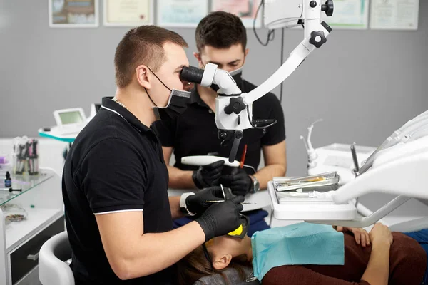 Αρσενικό οδοντίατρος εκτελεί μια οδοντιατρική checkup με τη βοήθεια του μικροσκοπίου, άλλο οδοντίατρο βοηθώντας τον να — Φωτογραφία Αρχείου