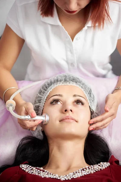 Brunette woman receiving electric ultrusound facial massage at beauty salon. Procedure in beauty clinic. Positive effects of physiotherapy. Close-up