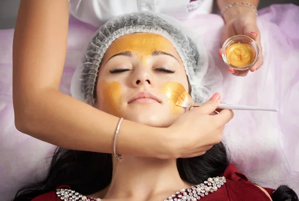 Kobiece kosmetyczki jest zastosowanie Złota Maska z miękką szczotką do piękna brunetka klienta salonu piękności. — Zdjęcie stockowe