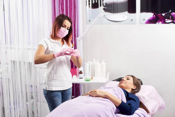 Profesional femenina en máscara rosa y guantes preparando una jeringa para iniciar un procedimiento a un joven cliente de un salón de belleza — Foto de Stock