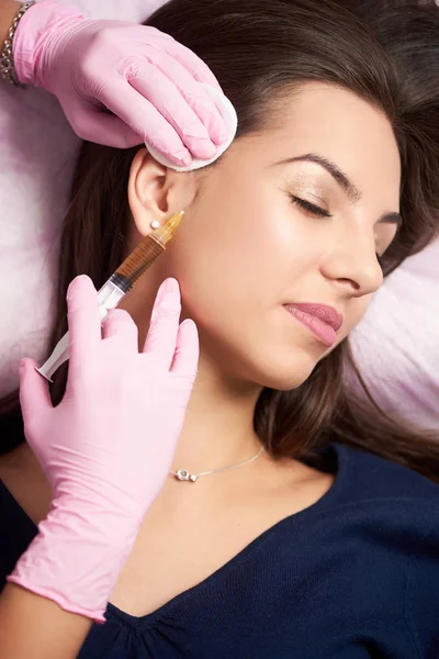 Inyección de jeringa realizada a una bonita clienta de un salón de belleza por un profesional en guantes rosados. Cosmetología y rutina de cuidado de la piel . — Foto de Stock