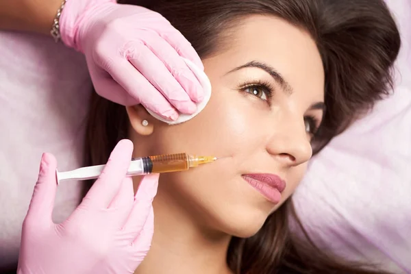 Close-up de mulher bonita recebendo injeção no salão de cosmetologia. Doutor em luvas médicas com seringa injeta droga bochechas . — Fotografia de Stock