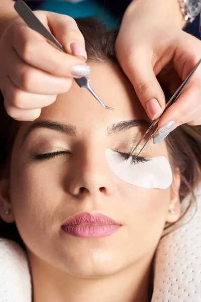 Procedimiento de extensión de pestañas. Primer plano de las manos de un esteticista con pinzas en las manos en el proceso de extensión de pestañas — Foto de Stock