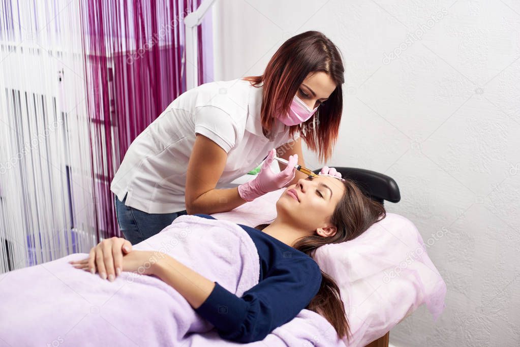 Filler injection for female forehead face. Plastic aesthetic facial surgery in beauty clinic. Beauty woman giving injections. Doctor in medical gloves and mask with syringe