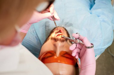 Genç erkek müşteri turuncu gözlük ile pembe eldiven bir doktor tarafından gerçekleştirilen diş enjeksiyon geçiriyor.