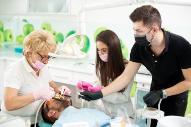 Diş hekimi bir kadın çalışıyor olan bir hastaya, iki yardımcı tarafından yardım etti: kız ve bir adam. Yeni teknolojilerle modern klinik