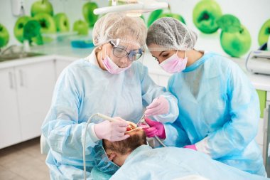 İki kadın diş hekimleri mavi elbiseler modern bir diş ofis erkek müşterisi diş tedavi.