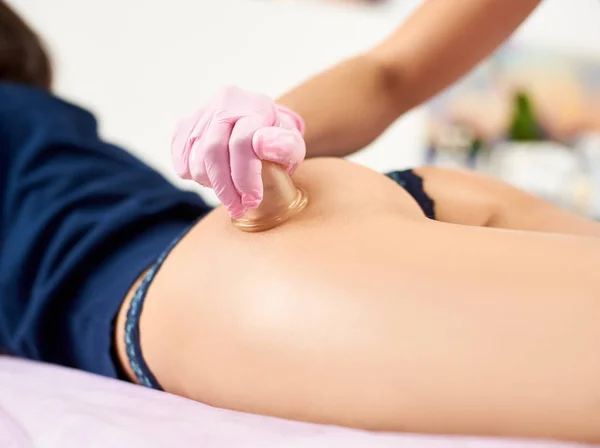 Primer plano de un masaje con ventosas realizado por un profesional en guantes rosados a una clienta femenina tonificada de un salón . — Foto de Stock