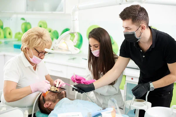 Zahnärztin arbeitet eine Frau mit einer Patientin, ihr stehen zwei Assistenten zur Seite: ein Mädchen und ein Mann. moderne Klinik mit neuen Technologien — Stockfoto