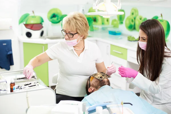 Zahnärztin bei der Arbeit an einem männlichen Patienten mit einem Casherdam. junge Assistentin hilft ihr in der Zahnmedizin im Krankenhaus mit neuen Technologien — Stockfoto