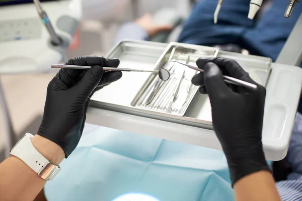 Das Makrofoto eines Zahnarztes in einem schwarzen Handschuh zeigt ein Werkzeug zur Behandlung des Patienten. das Konzept der modernen Zahnmedizin — Stockfoto