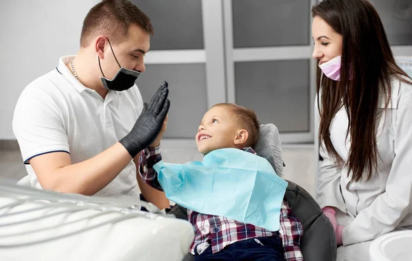 Αρσενικό ο οδοντίατρος και ο Βοηθός του με υπέροχο παιδί μετά τη θεραπεία των δοντιών στο οδοντιατρείο γραφείο, χαμογελαστός και δίνοντας παραπέρα. — Φωτογραφία Αρχείου
