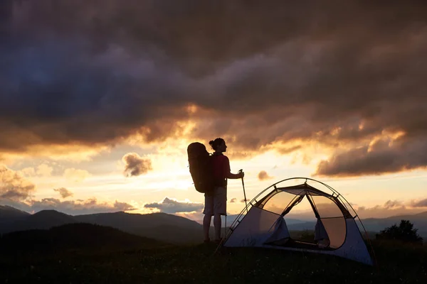 Fotografía horizontal de una silueta de una mochilera de pie cerca de su tienda en las montañas observando la hermosa puesta de sol copyspace viajar turismo estilo de vida activo naturaleza . — Foto de Stock