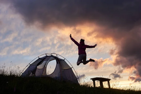幸せな女が興奮して高くジャンプします。山の中で日没 copyspace テント キャンプ場レクリエーション週末自然調和感情幸せ満喫キャンプ夕暮れの風景 — ストック写真