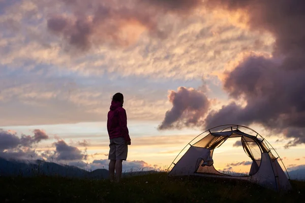 Siluett av ung kvinna som står nära läger med vacker natur solnedgång på berget med varmt ljus som semester camping eller koppla av eller glad koncept — Stockfoto