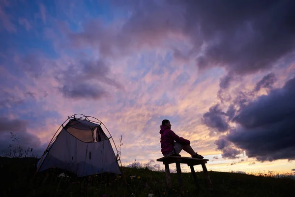 Cielo púrpura. Joven turista disfrutando de la impresionante puesta de sol cerca de la tienda de campaña en las montañas en Rumania. Nubes mujer chica escalador naturaleza magnífico increíble maravilloso paisaje paisaje pendiente — Foto de Stock