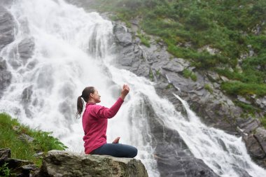 Balea Fagarash Dağları'nda bir şelale altında dağ havası gidiyor bir lotus poz profilde kız oturuyor