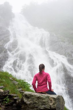 Kayanın üzerinde rahatlatıcı ve şelale Balea Fagarash dağlarda güzel manzarayı turist kız. Karpatlar Romanya, Transfagarasan road yakınındaki yer. Arkadan Görünüm