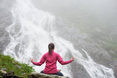 Söz konusu genç erkek kaya Romanya'da muhteşem Balea şelale önünde yoga pratik üzerinde meditasyon. Kadın çekici sağlıklı yaşam yogini nefes kesen sahne doğa turizm şaşırtıcı