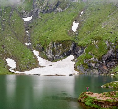 İnsanlar ve doğa. Kadının doğa büyüklüğü için karşılaştırıldığında küçük bir rakam. Yeşil taşlar ve Romanya Vidraru Gölü yakınındaki çayır. Şaşırtıcı görünümü sahne eller yukarı kadın kar dağ güzel manzara