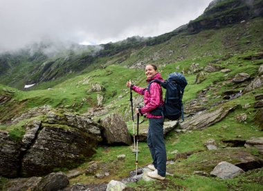 Mutlu kadın turist Romen dağlar Vadisi'da yürüyüş hareketi ile parmak sınıfı gösterir. Sırt çantası ve trekking sopa kadın ile