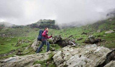 Sopa ve sırt çantası trekking ile kadın backpacker Romanya dağlarında tırmanıyor. Bulutlar dağlar kefene