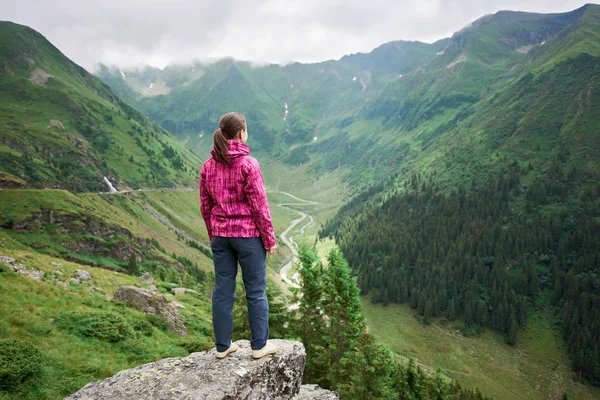 Turistul feminin se bucură de peisajul frumos al văii munților verzi, norii atârnați peste ei și Autostrada Transfagarashan. Cel mai frumos drum din Europa, România — Fotografie, imagine de stoc