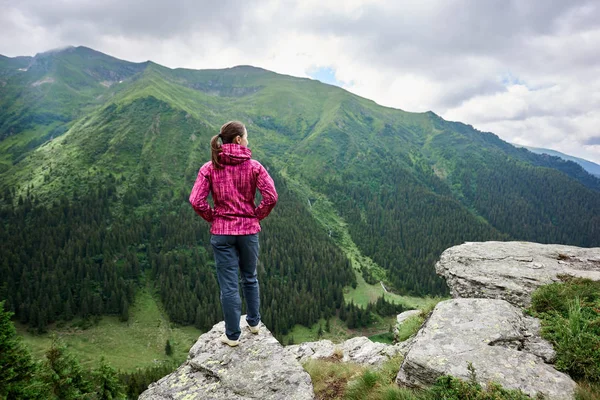 Vista trasera de una niña de pie en un acantilado frente a su apertura de un paisaje fascinante de poderosas montañas verdes y nubes por encima de ellos. Europa, Rumanía — Foto de Stock