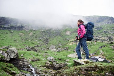 Sırt çantası konumu bir kaya üzerine olan genç kadın turist boşaltmak çevresinde muhteşem dağ manzarası zevk rahatla dinlenme kamp uzun yürüyüşe çıkan kimse hobi yaşam tarzı zevk doğa.