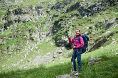 Genç mutlu famele hiker trekking sopa ve bir sırt çantası ile Fagaras dağlar, Romanya'nın eteklerinde bir taş üzerinde duruyor. Kameraya gülümseyen ve gösterilen kız yaşasın
