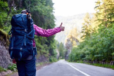 Romanya çimenli kayalık tepede çevrili boş dağ yolda otostop kadın turist. Adam yeşil ağaçlar yamaç yolunu seyahat güneşli sağlıklı yaşam kadın dağcı sırt çantası bulanık