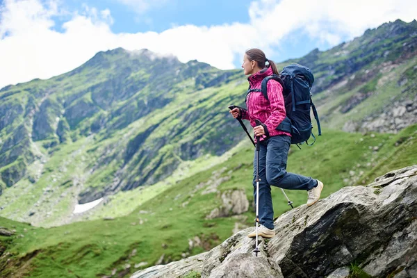 Молодая женщина с рюкзаком спускается по скалистой местности с размытым видом на могучие зеленые горы и голубое небо с облаками. Горы Фагарас, Карпаты, Румыния — стоковое фото