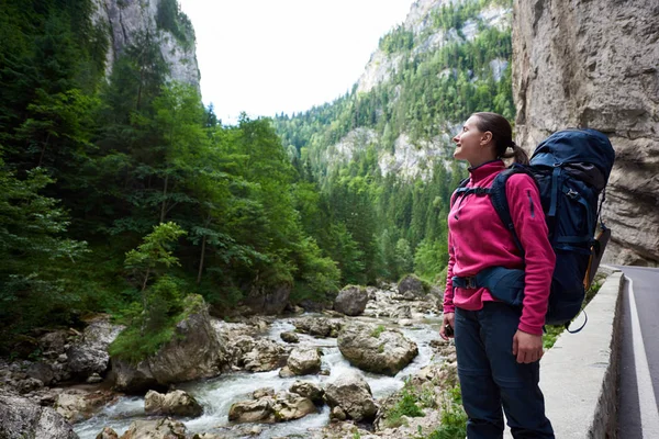 O femeie alpinist pozitiv admirând priveliștea uimitoare a munților stâncoși verzi și a fluxului de apă din zona montană din România. Femeie turist zâmbet fericit rucsac deal copac piatră stil de viață sănătos — Fotografie, imagine de stoc