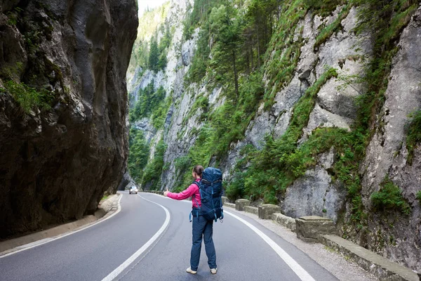 Femeia turistică cu rucsac prinde o mașină pe drum în Cheile Bicazului. Canionul Bicaz este unul dintre cele mai spectaculoase drumuri din România. Pasaj montan spectaculos în Transilvania . — Fotografie, imagine de stoc