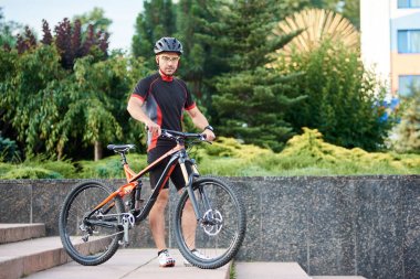 Adam profesyonel motorcu beton merdiven yanında yeşil ağaçlar ve bahçenizi bisikletle yakın poz. Sağlıklı yaşam, eğitim açık havada, çekim sport reklam kavramı