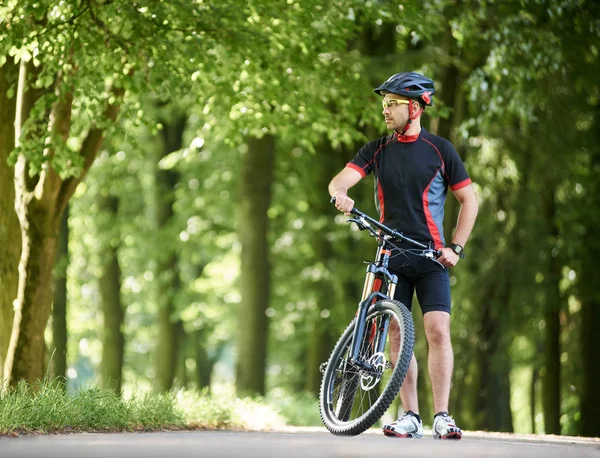 英俊的男车手在专业运动服服装和防护头盔看远距离休息从骑在绿色公园 运动员户外训练 欣赏大自然 — 图库照片