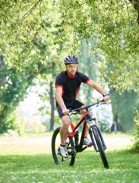 骑自行车的年轻人骑单车服和防护头盔 沿着绿色公园小巷骑车 运动员在户外训练 健康生活方式概念与自然的联系 — 图库照片