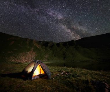 Işıklı turuncu çadır. Gece yıldızlar ve parlak Samanyolu ile mayınları inanılmaz güzel gökyüzü altında göl yakınındaki dağlarda kamp.