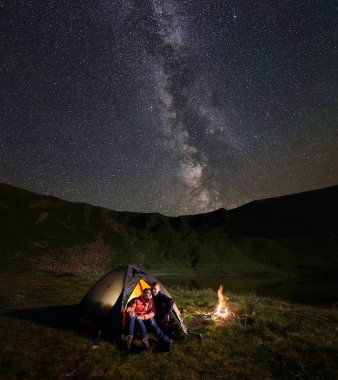 Genç çift backpackers bir dinlenme ışıklı çadırda kamp ateşi, kamp, inanılmaz yıldızlı gökyüzü parlak Samanyolu ile zevk gece sahip kucaklayan.