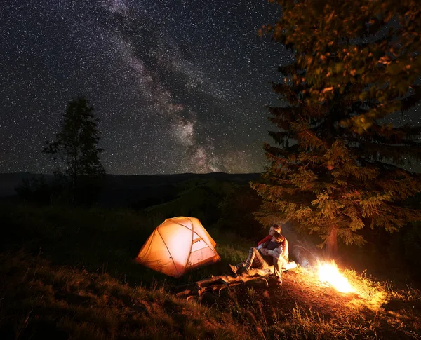 Romantische Paar Wanderer Sitzen Auf Baumstämmen Neben Beleuchteten Orangefarbenen Zelt — Stockfoto