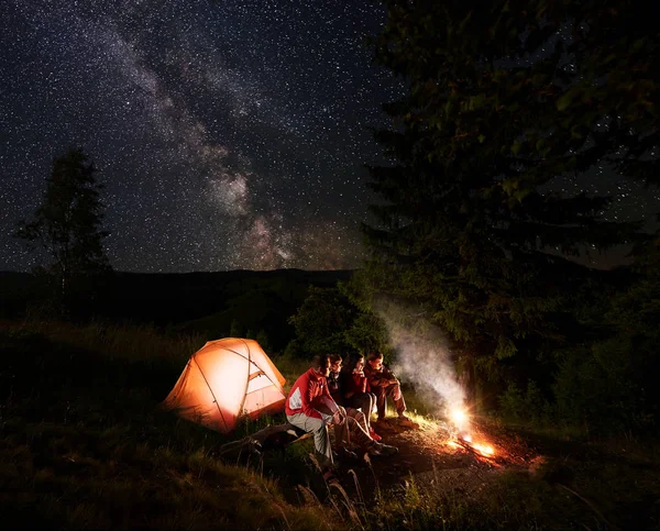 Cuatro Amigos Excursionistas Descansando Tronco Cerca Carpa Naranja Iluminada Disfrutando — Foto de Stock